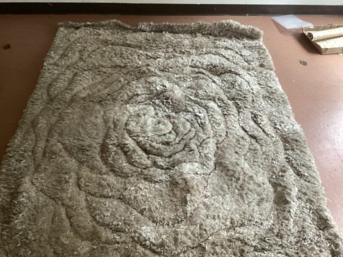 A high-pile beige shag rug with a sculpted 3D rose pattern, completely deep-cleaned, sanitised for pet odours, and pile-restored to eliminate furniture marks on a workshop floor.