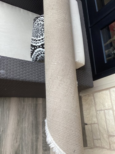 A rolled-up residential rug showing visible nap distortion and uneven texture, indicative of wear and in need of professional cleaning and restoration.