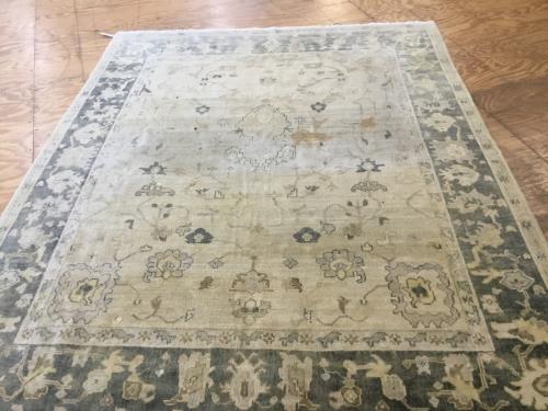 Before cleaning, an ornate residential area rug with visible black coffee stains on a hardwood floor, ready for professional cleaning by Dalworth Rug Cleaning.