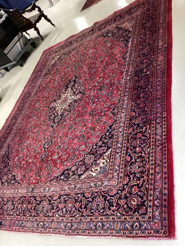 An expansive traditional Persian area rug featuring an ornate red and navy floral medallion pattern, completely deep-cleaned, treated for colour bleeding, and restored to a plush finish on a facility floor.