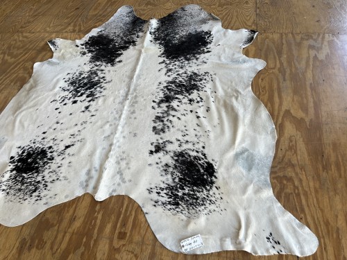 A clean black and white speckled cowhide rug, professionally treated for faded areas and heavy soil by Dalworth Rug Cleaning, lying on a wooden floor.