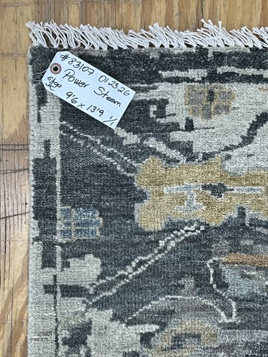 Close-up view of a commercial area rug with a dark and light abstract pattern, showing a tag indicating 'Power Steam' cleaning service.