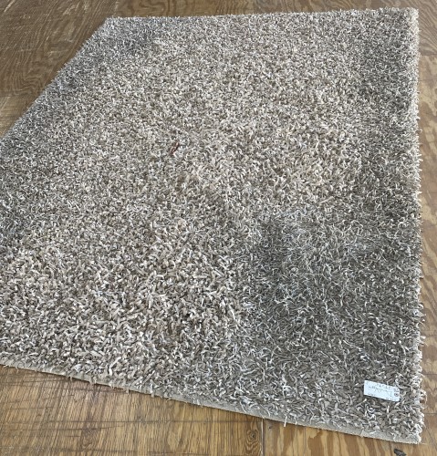 Before professional residential rug cleaning, a dirty, shaggy beige area rug requiring deep cleaning.