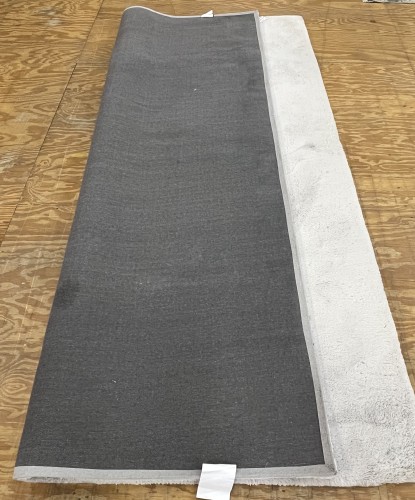 Underside of a light-colored residential rug laid out on a wooden floor for inspection before cleaning.