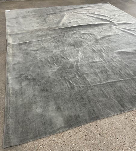 Large grey commercial rug fully laid out on a concrete floor, showcasing the results of professional commercial rug cleaning by Dalworth Rug Cleaning.