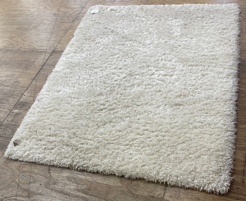 A pristine, freshly cleaned cream-colored shag area rug lying on a light wooden floor after professional residential rug cleaning.