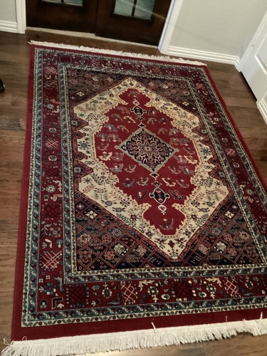 A large traditional Persian area rug with an intricate crimson field, cream diamond medallion, and geometric borders, completely deep-cleaned, treated for pet odours, and pile-restored on a hardwood floor.