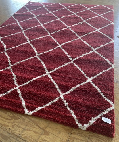 Full view of a residential red shag rug with white diamond patterns on a wooden floor, before professional cleaning by Dalworth Rug Cleaning.