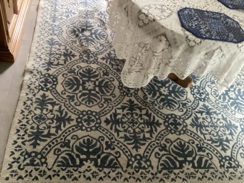 Residential rug with white and blue patterns showing white knots and moderate soil before professional cleaning.