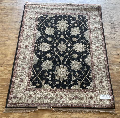 Full view of a cleaned Robert Jacobs residential rug featuring intricate black and beige floral patterns with a decorative border, laid flat on a wooden surface.