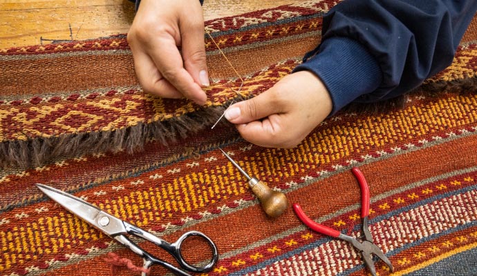 Person repairing rug with sewing equipment