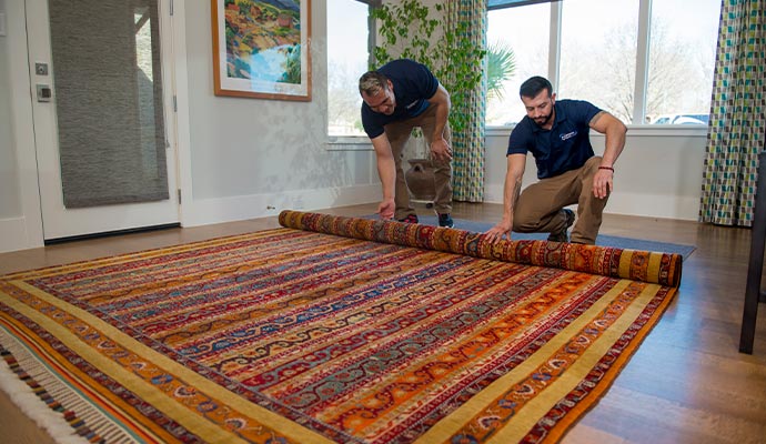 Technicians carefully rolling an area rug inside a home