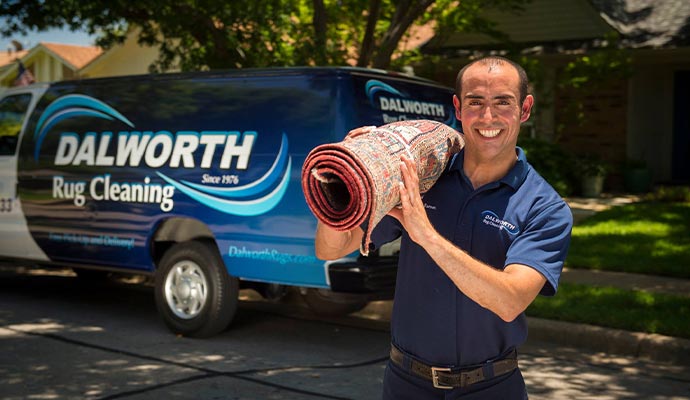 A smiling technician carrying a rolled area rug toward a branded service van for safe transport to our cleaning facility