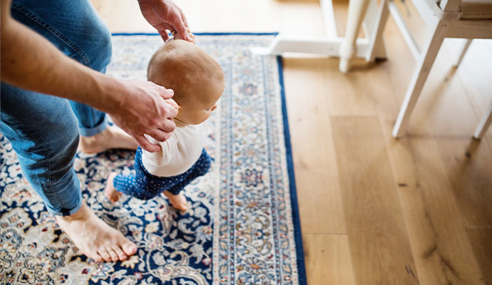 A person playing with a baby on a clean rug in a fresh indoor environment