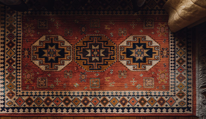 An overhead view of a clean red and orange patterned indoor area rug with tribal designs on a wood floor