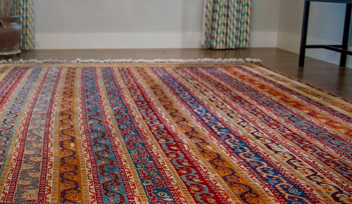 A close-up of a high-quality rug pad installed under a decorative red indoor rug for cushioning and floor protection
